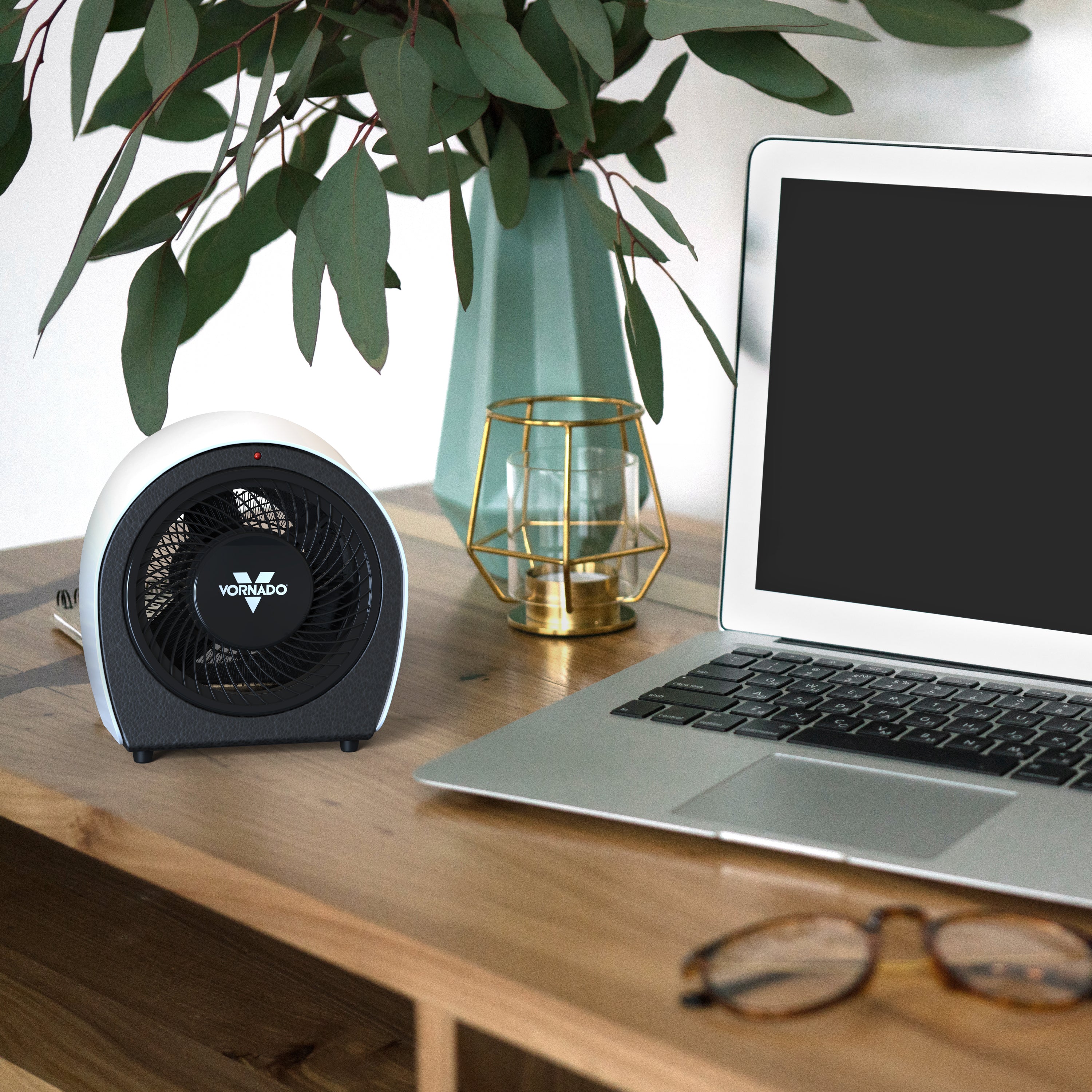 Laptop on a desk with a heater, glasses, and decorative items.