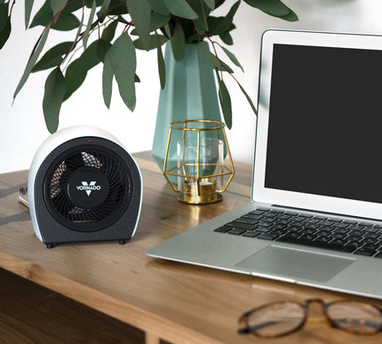 Laptop on a desk with a heater, glasses, and decorative items.