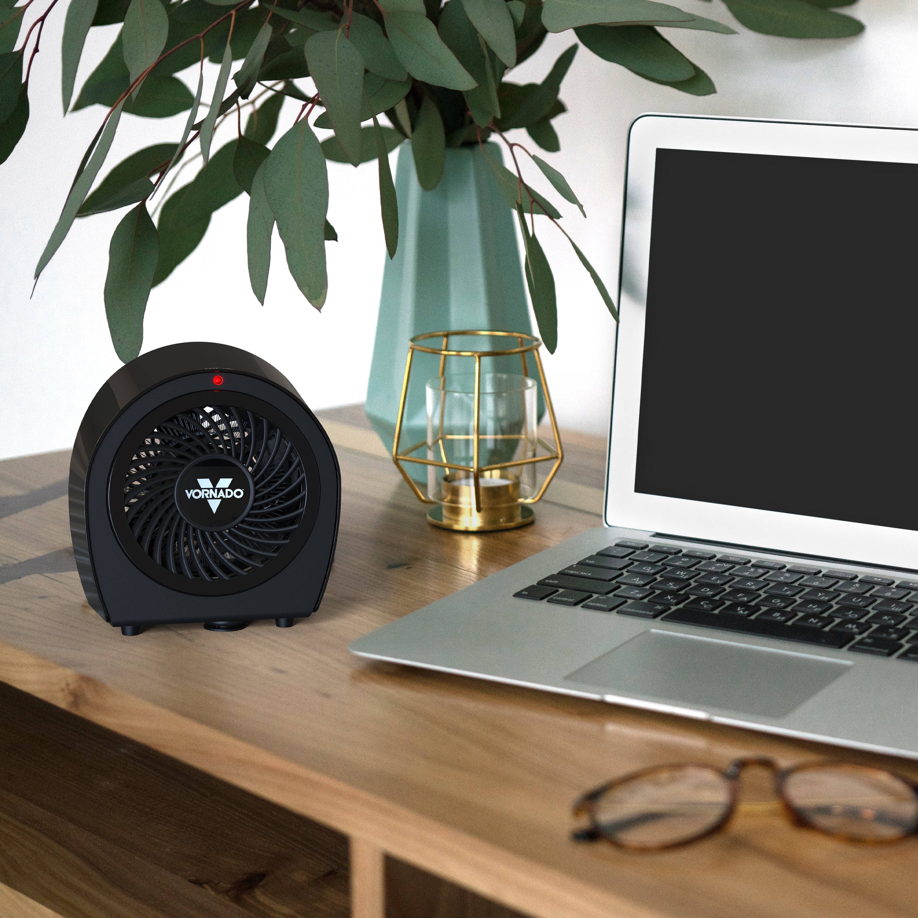 Black heater on a desk next to a laptop, plant, and glasses