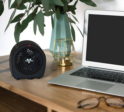 Black heater on a desk next to a laptop, plant, and glasses