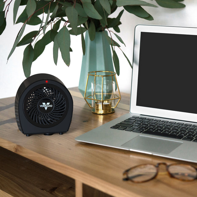 Black heater on a desk next to a laptop, plant, and glasses