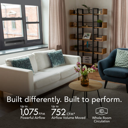 Modern living room with white sofa, blue armchair, and decorative elements. A vornado window fan is being used in the back window