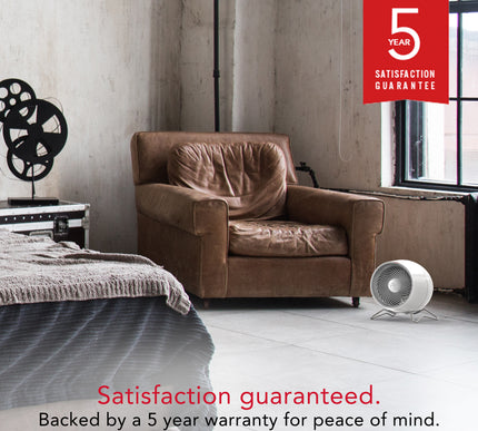 Brown armchair in a room behind a white Vornado heater with a 5-year satisfaction guarantee badge.