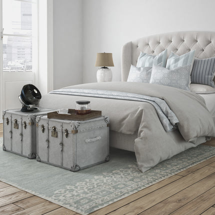 Neatly made bed with gray bedding in a bedroom setting with a black fan on a table