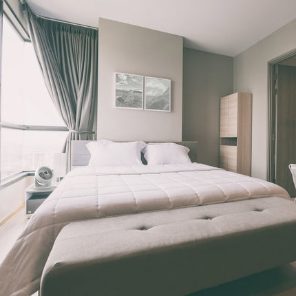 Neatly made bed in a modern bedroom with light decor and white fan on nightstand