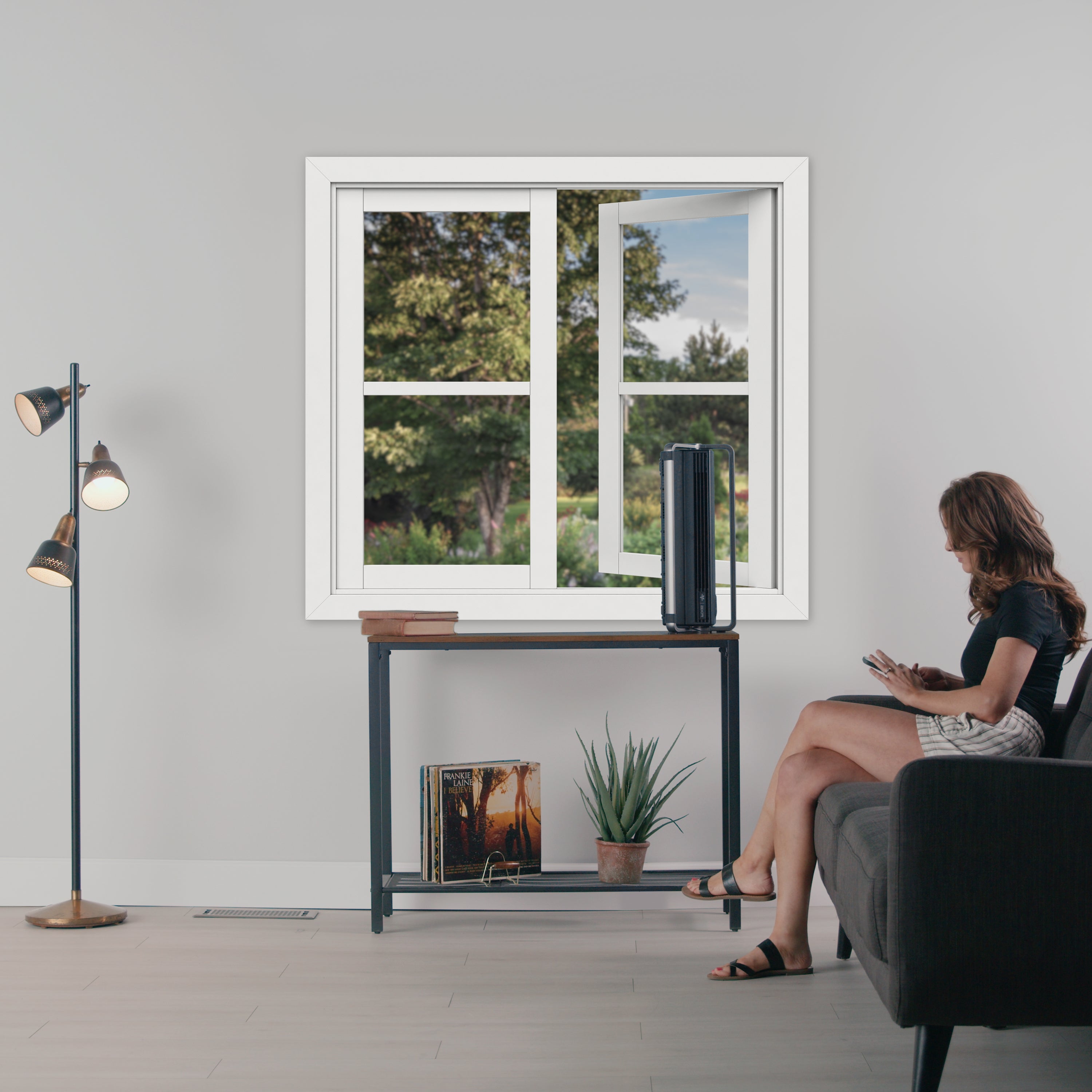 Black air circulator on table in living room with person sitting on black couch