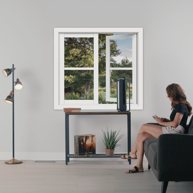 Black air circulator on table in living room with person sitting on black couch