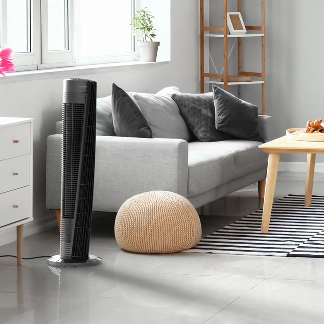 Tall black tower fan in a modern living room with a sofa and decor.