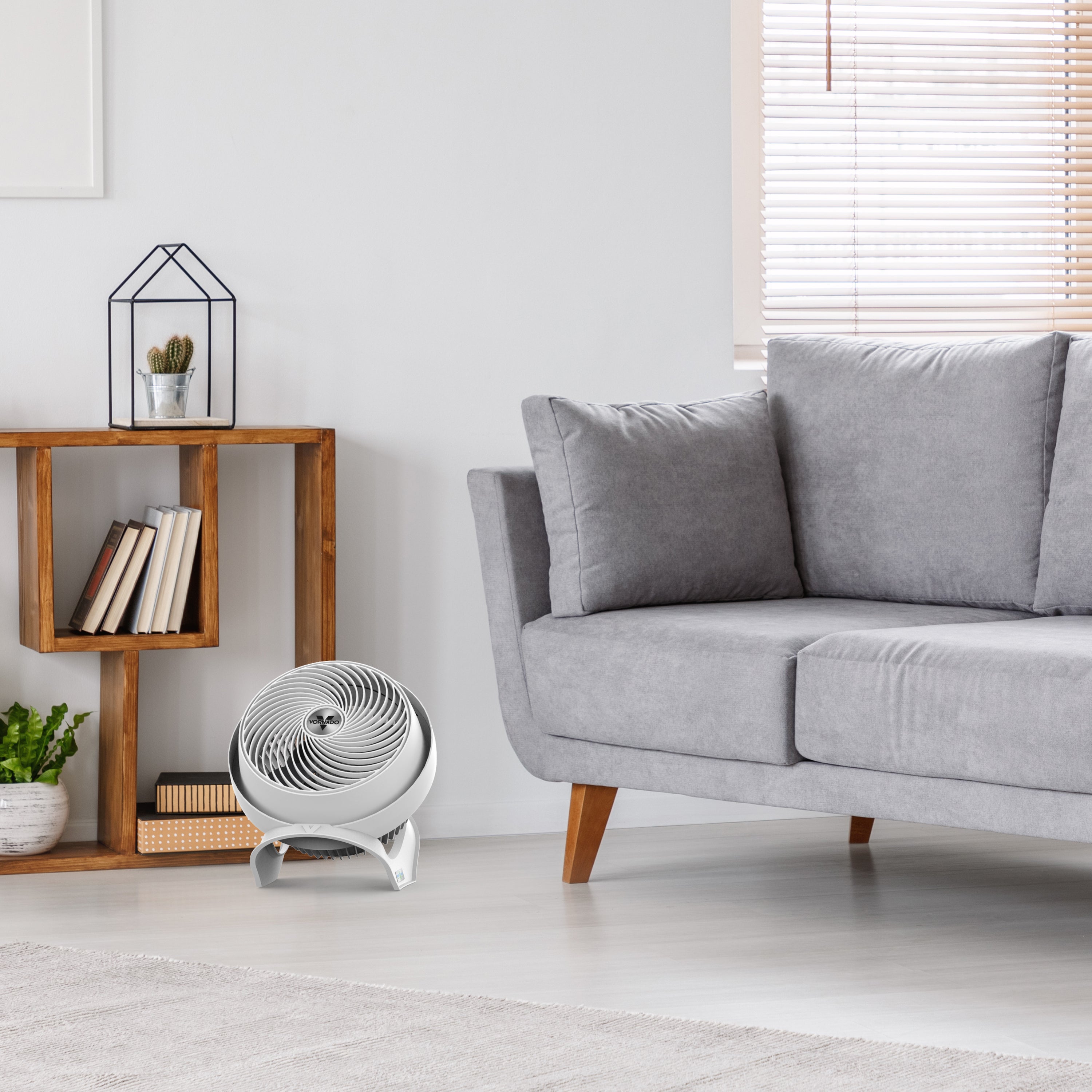 Modern living room with a gray sofa, wooden side table, and floor fan.
