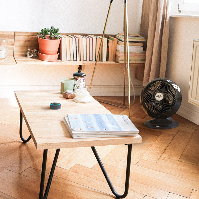 Wooden coffee table with books and a fan in a room with a shelf and decor.