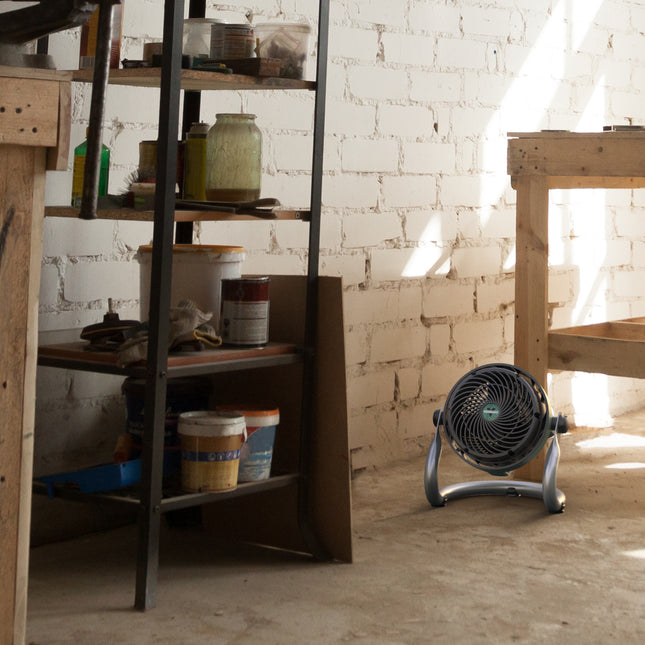 Room with a shelf and a floor fan in front of a brick wall