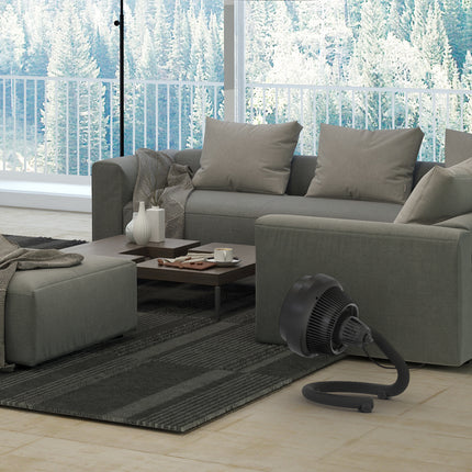 Gray sectional sofa in a living room with a window view of trees, featuring a black portable fan on the floor.