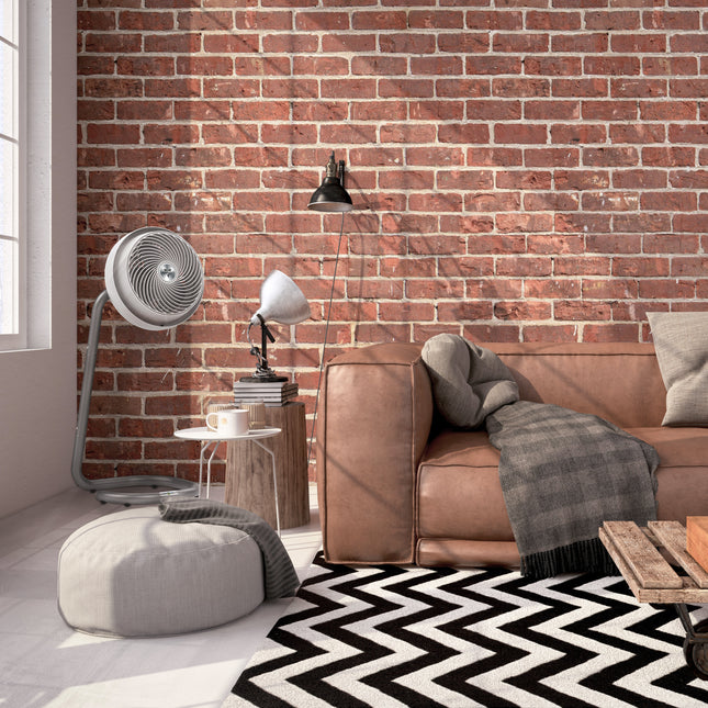 Living room with brown leather sofa, gray pouf, and brick wall.