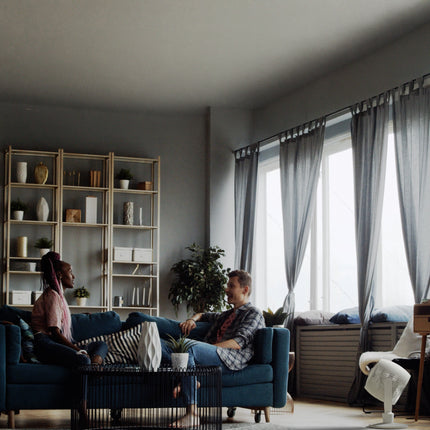 Two people sitting on a blue couch in a modern living room with large windows.