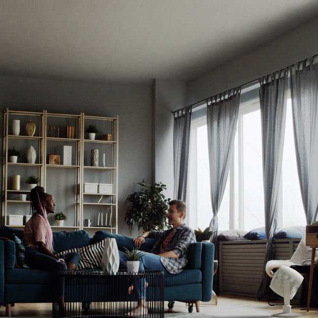 Two people sitting on a blue couch in a modern living room with large windows.