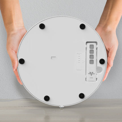 Round electronic device held by hands against a light gray background