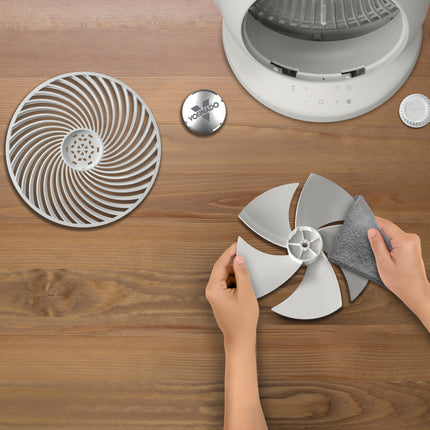 Person cleaning a fan blade with a cloth on a wooden surface