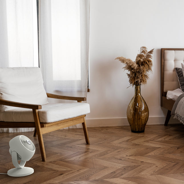 Modern room with a chair, vase, and fan on a wooden floor.