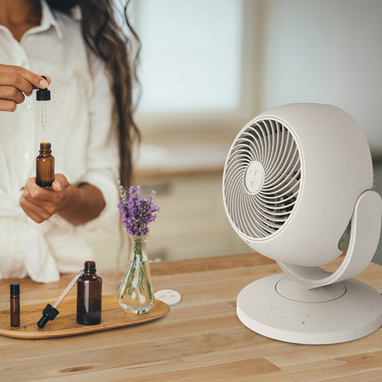 Person holding a dropper bottle with essential oils next to a white fan on a wooden surface.