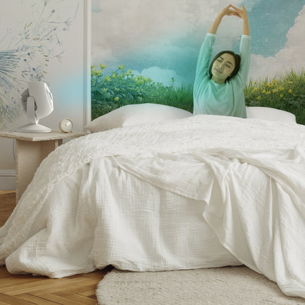 Woman stretching in bed with a scenic wall mural of a field and sky.