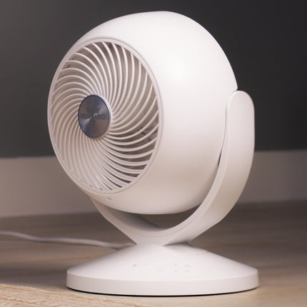 White desk fan on a wooden surface with a dark background