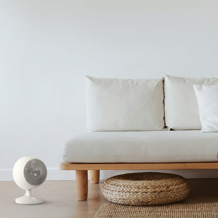 Minimalist living room with a white sofa, woven ottoman, and small white fan.