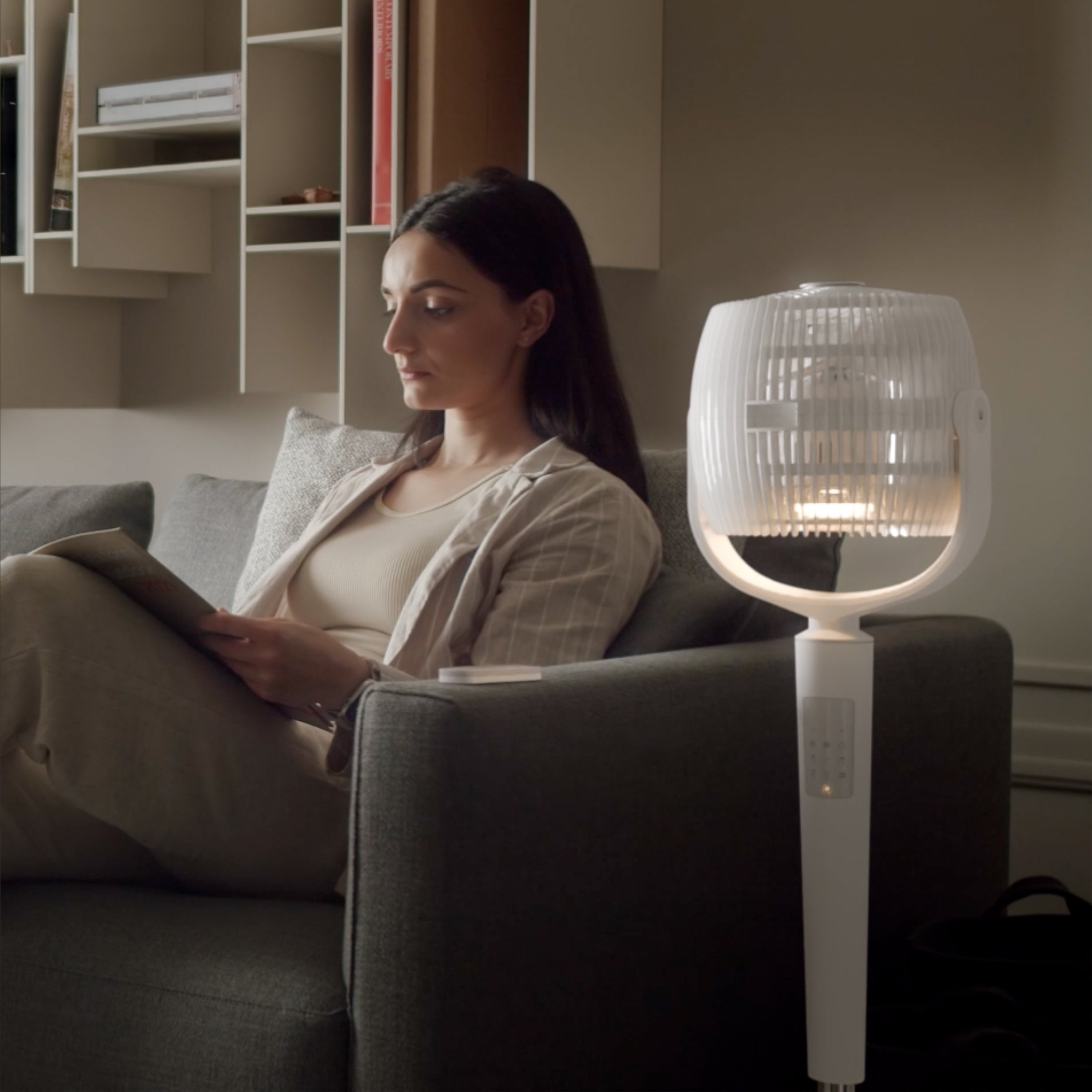 Woman sitting on a couch reading a book with an EOS 9S in lamp mode next to her.