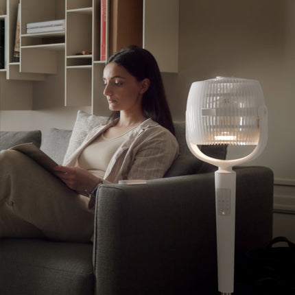 Woman sitting on a couch reading a book with an EOS 9S in lamp mode next to her.