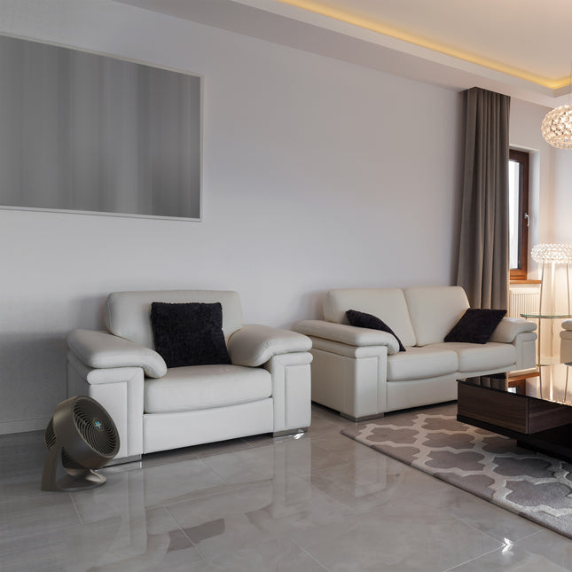 753 in a living room in front of a white chair and across from a white couch. The fan sits on a floor made of a reflective tile