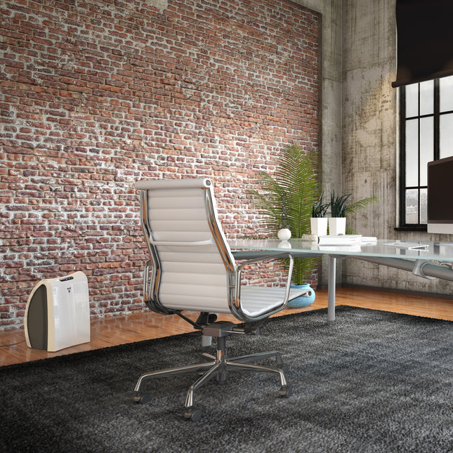AC350 against a brick wall in a modern office and directly next to a desk, computer, and chair set up with a tall plant in the distant corner of the room