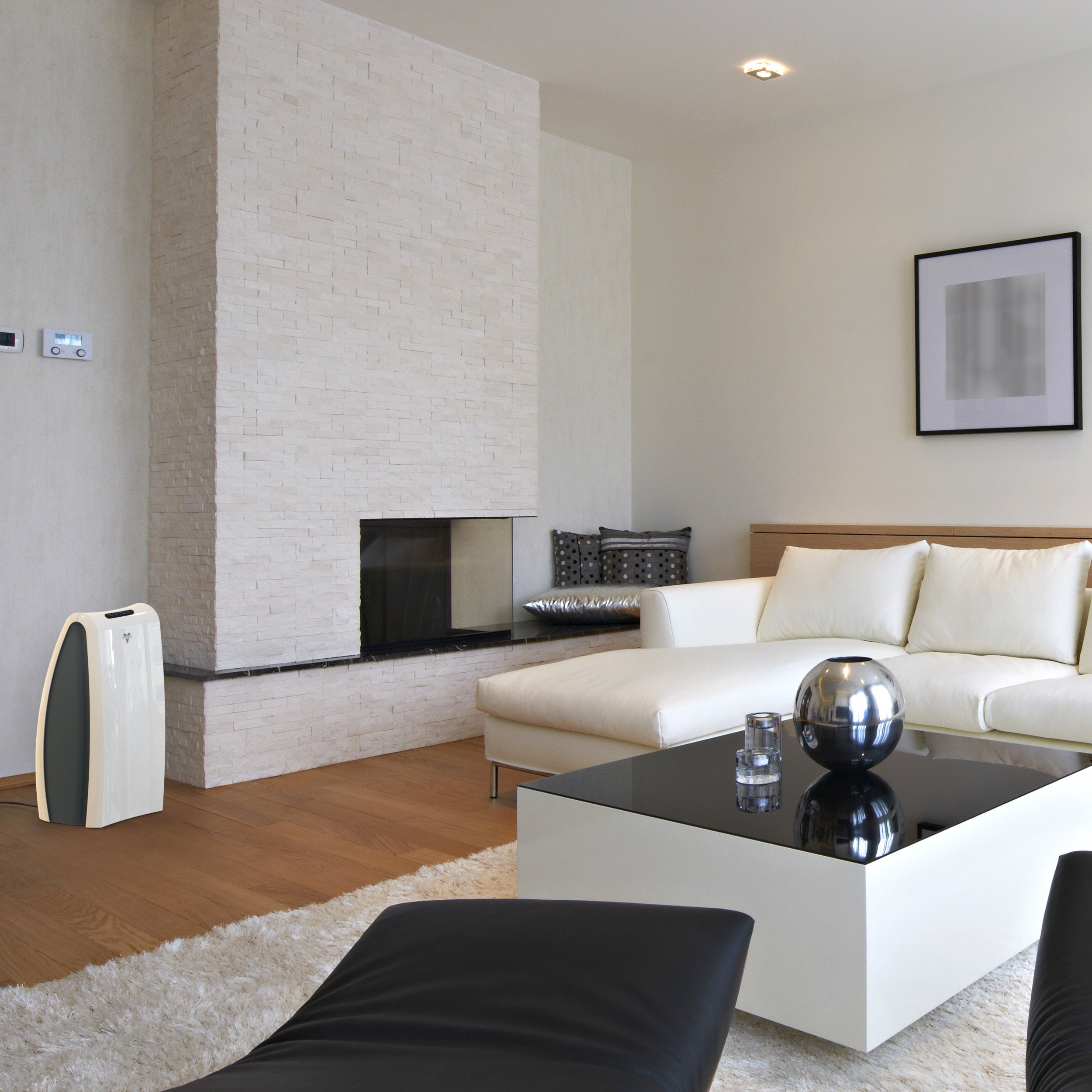 AC550 against a white wall and next to a brick fireplace in a living area. The air purifier faces a white couch and coffee table