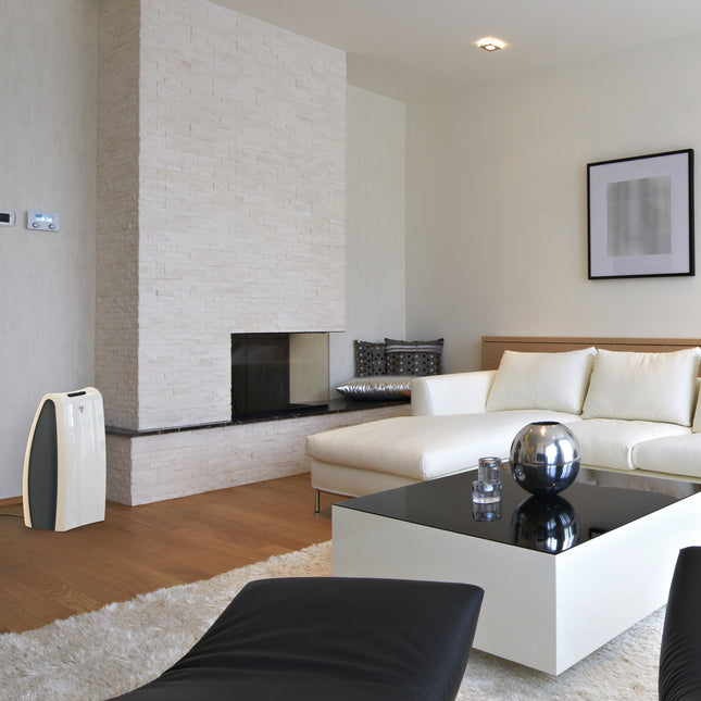 AC550 against a white wall and next to a brick fireplace in a living area. The air purifier faces a white couch and coffee table