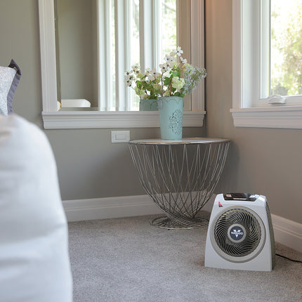 AVH10 on a carpet floor in a bedroom facing a bed with windows behind the heater filling the room with natural lighting