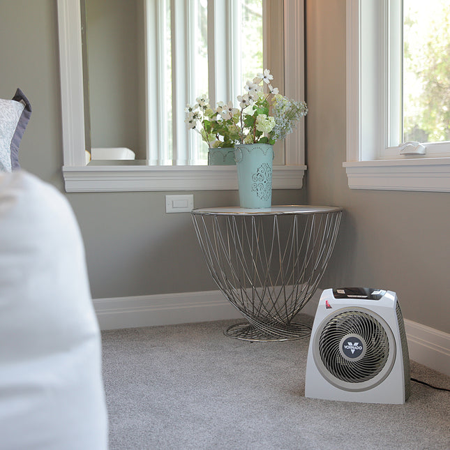 AVH10 on a carpet floor in a bedroom facing a bed with windows behind the heater filling the room with natural lighting