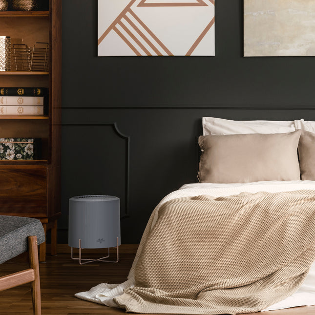 cylo51 air purifier in a bedroom with a dark gray wall accent next to a bed and wood shelf with books and decor