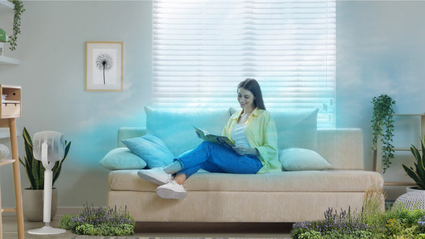 Woman sitting on couch with EOS 9S to her right. A blue sky is on the wall and wild flowers are on the floor to indicate breeze mode.