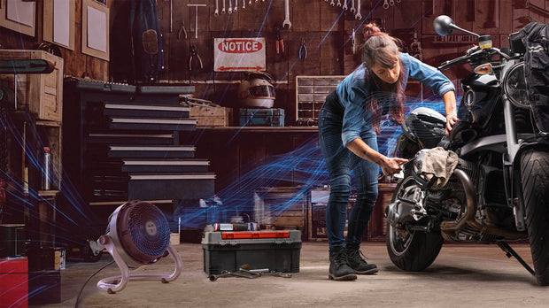 Woman working on motorcycle in garage as EXO61 circulates air throughout the whole room.
