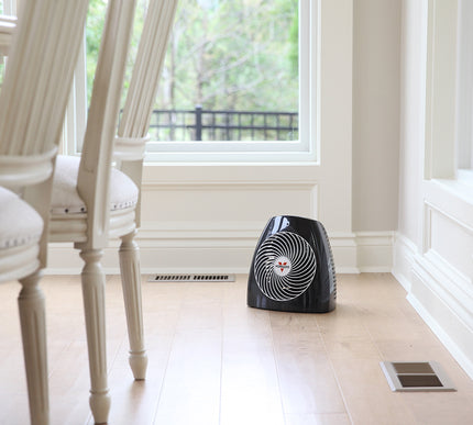 MVH heater in the corner of a dining room facing a table and chair with large windows behind it on a hardwood floor