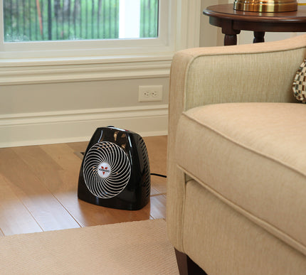 MVH in a living room next to a tan couch on hardwood floors with white designed baseboards and natural room lighting