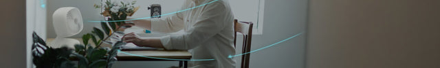 A man sitting at a desk in a small room. Movio 6 is in front of him, blue arrows are coming out of the circulator, indicating small room circulation.