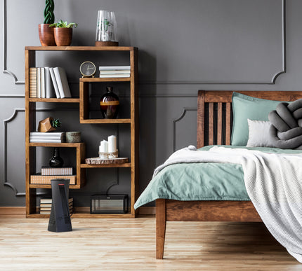 oscth1 in a bedroom on wood floors facing a wood-framed bed with room decor on a wooden shelf behind the heater