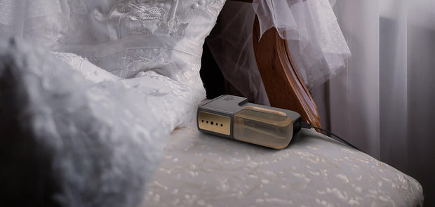 The passport handheld garment steamer next to a laid out wedding dress on a chair.