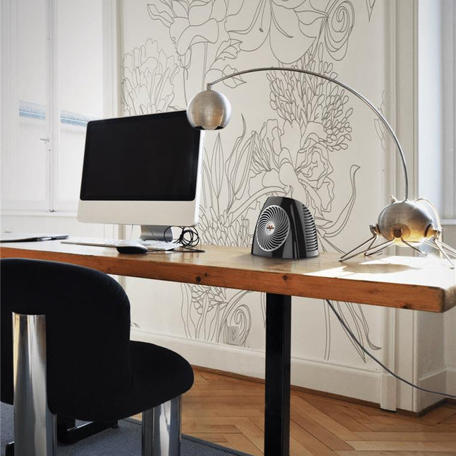 VH202 heater on a wooden desk with a white wallpaper backdrop and wood floors. Next to the heater is a white desktop computer setup and black office chair