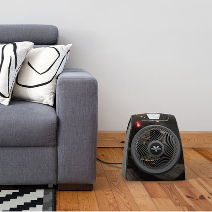 Black space heater on a wooden floor next to a gray sofa with decorative pillows.