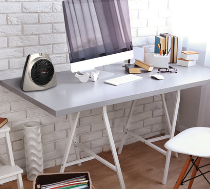 VH203 personal space heater on an office desk with a white brick wall backdrop and a computer setup with various books on the desk