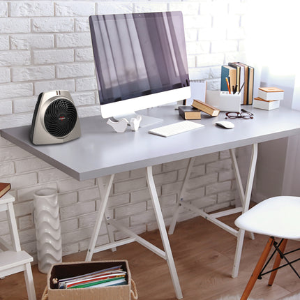 VH203 personal space heater on an office desk with a white brick wall backdrop and a computer setup with various books on the desk