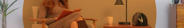Woman reading in her chair with the VH204 heater on the side table. There is an orange circle overlay on her to indicate spot heat on low.