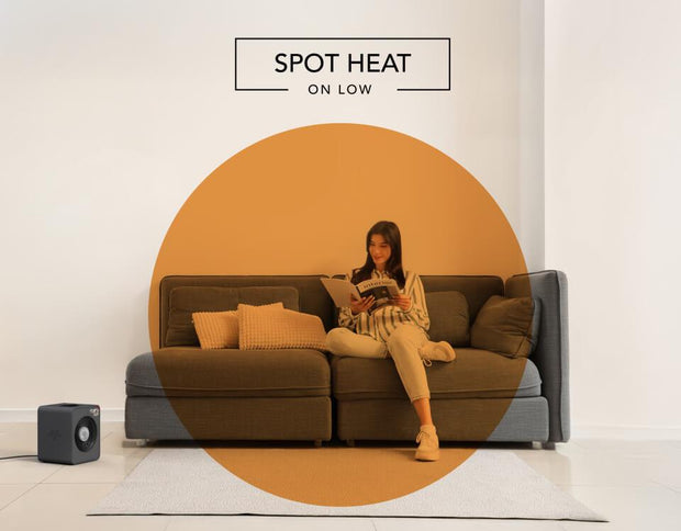 Woman reading on her couch with the VMHi300 heater on the floor. There is an orange circle overlay on her to indicate spot heat on low.