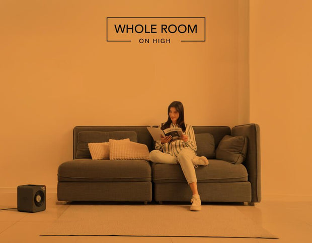 Woman reading on her couch with the VMHi300 heater on the floor. There is an orange overlay to indicate whole room heat for a small room on high.