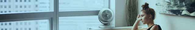Woman sitting on a couch by a large window as Vora 8 circulates air throughout the room.